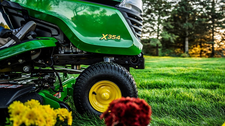 Close up of the X354 model logo on a green riding mower hood with flowers in the foreground.
