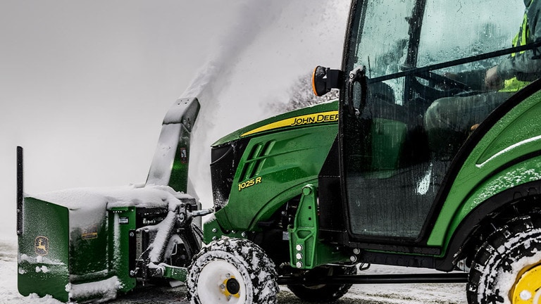 A green compact tractor with a front-attached snow-blower removing snow from a path. (10th thumbnail)