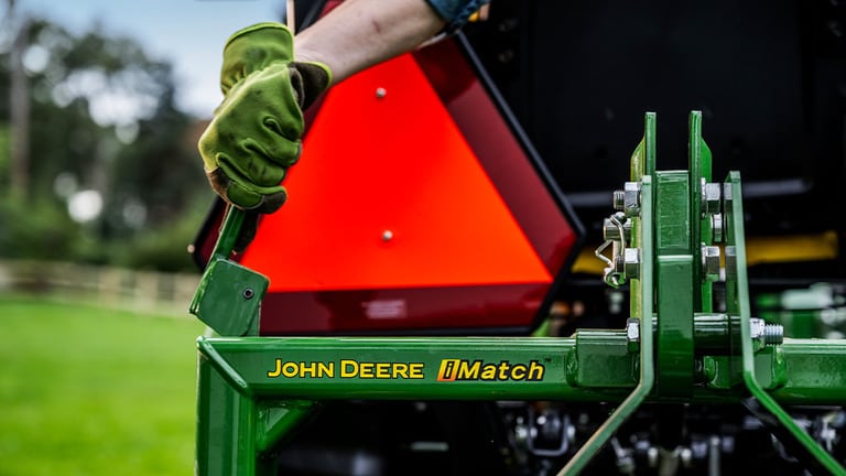A gloved hand pulls a lever in front of the rear SMV emblem near the John Deere iMatch logo. (13th thumbnail)