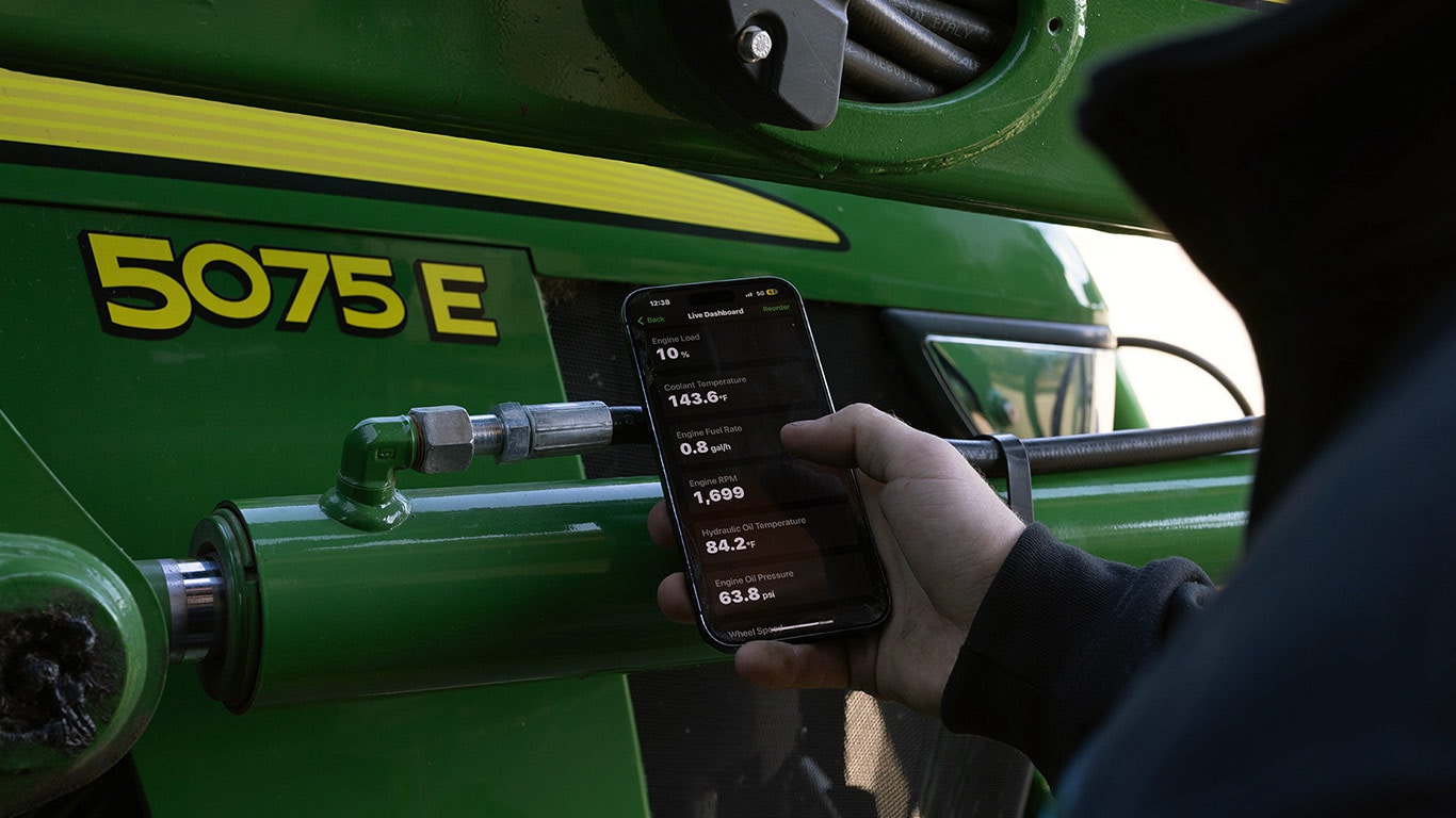 hand holding a cell phone with an app in front of a green and yellow tractor hand holding a cell phone with an app in front of a green and yellow tractor