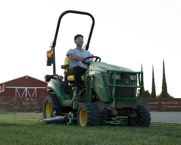 person mowing with a green and yellow compact tractor and a barn in background