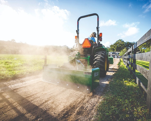 person driving green and yellow compact tractor down a dirt driveway