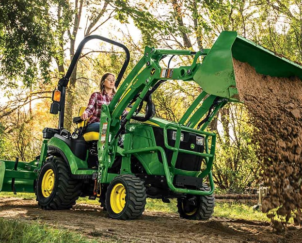 person dumping dirt with green and yellow compact tractor