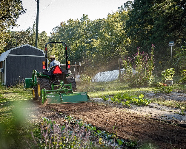 person driving green and yellow compact tractor preparing soil
