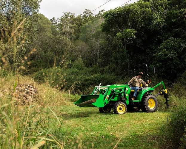 person using post-hole digger with green and yellow compact tractor