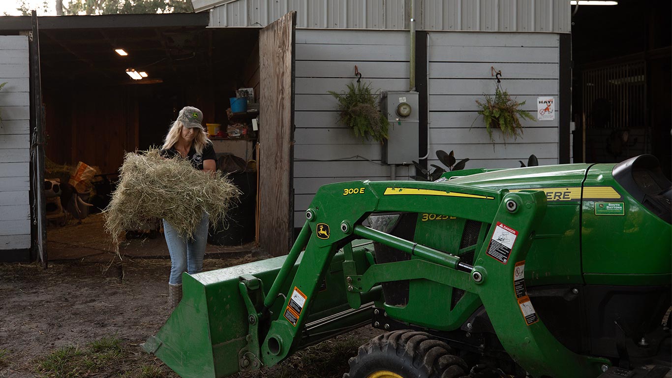person carrying hay to a green and yellow compact tractor person carrying hay to a green and yellow compact tractor