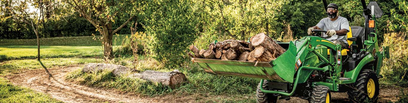 person on a tractor carrying logs with trees in background