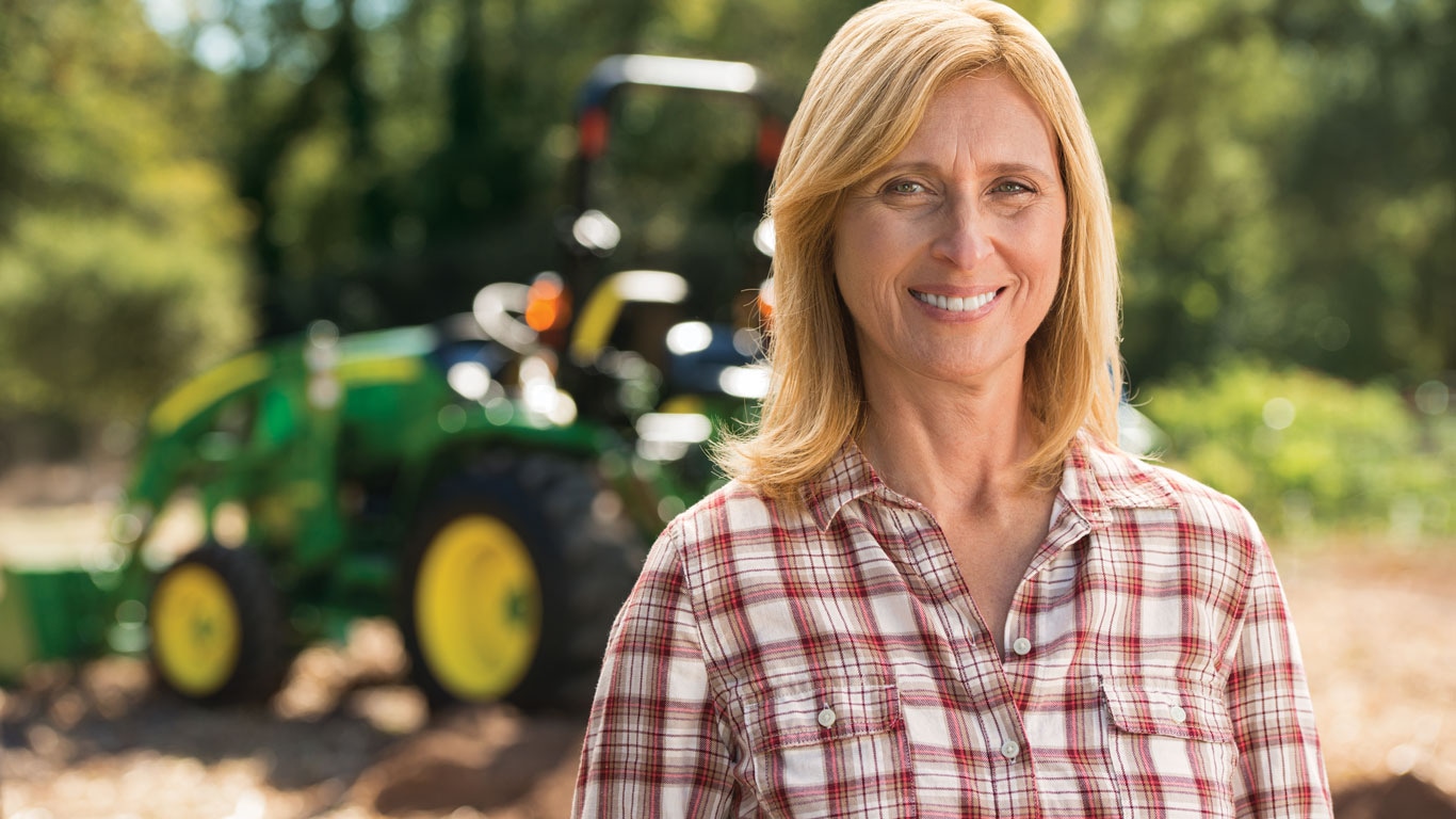 a woman smiling with a compact tractor in the background