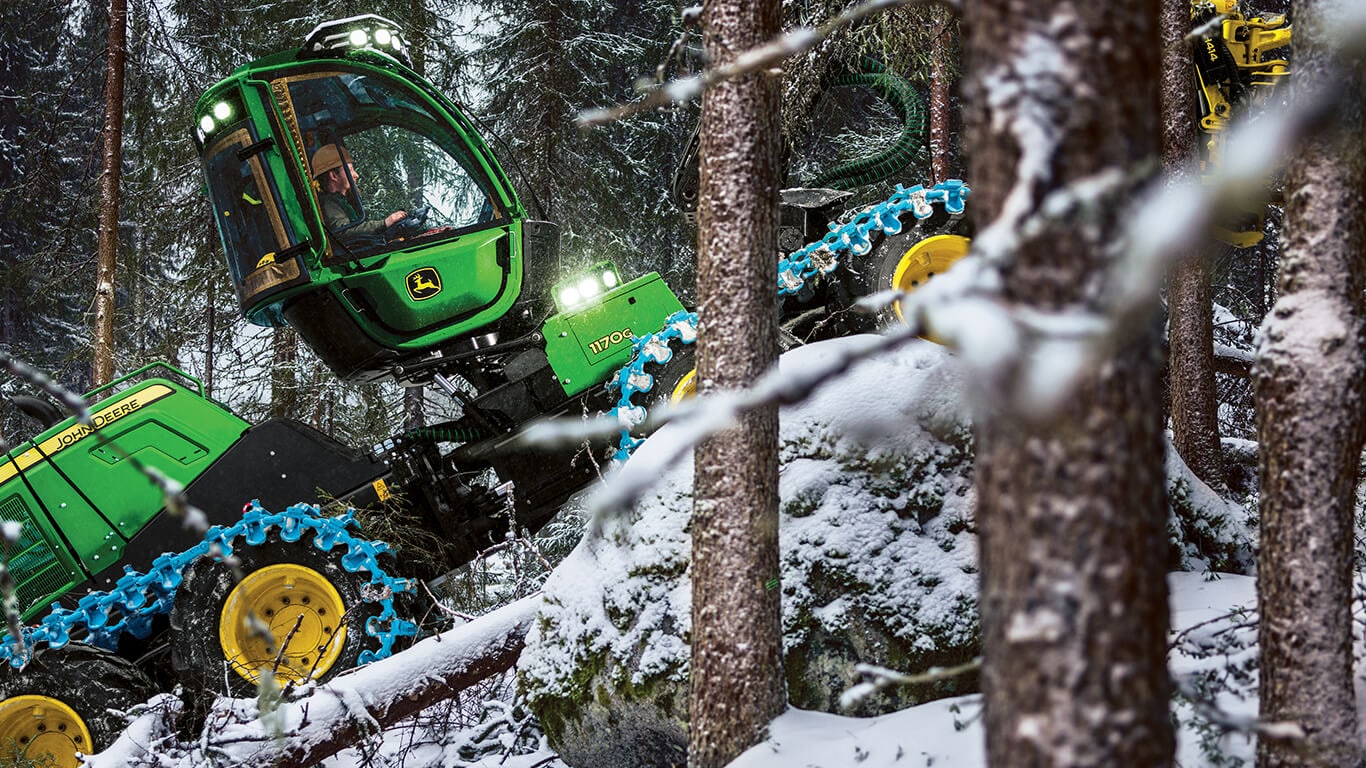 1170G wheeled harvester driving uphill in snowy wooded area.