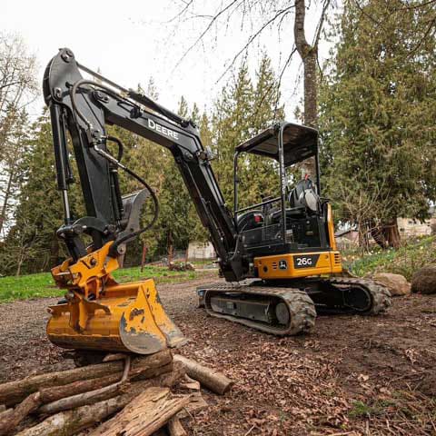 a John Deere 26G mini excavator works on a pile of logs