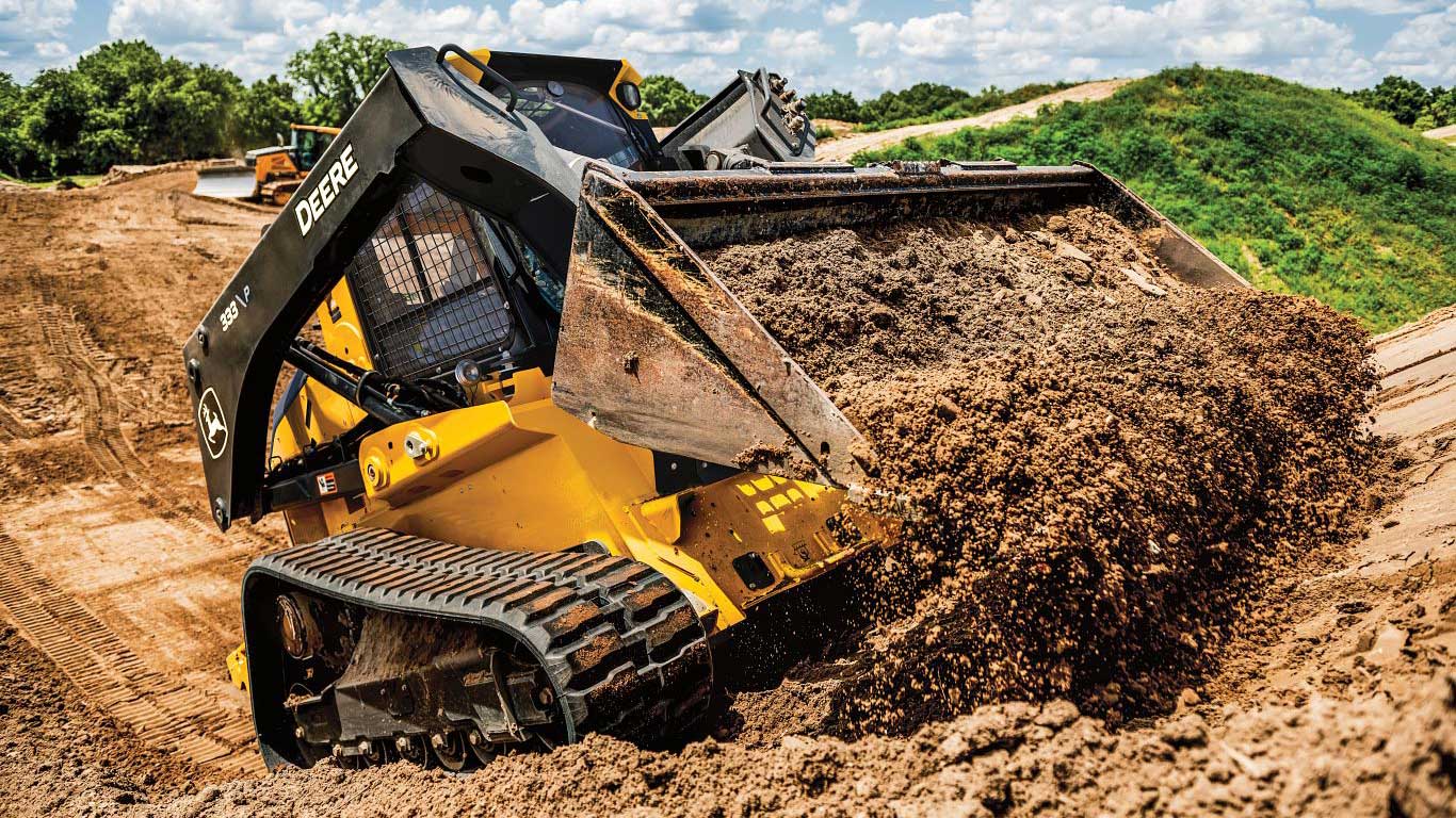 333 P-Tier Compact Track Loader unloads a bucket of dirt on a sloped hill