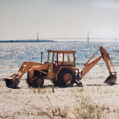 A John Deere 410 Backhoe sitting on the beach in front of the Golden Gate Bridge.