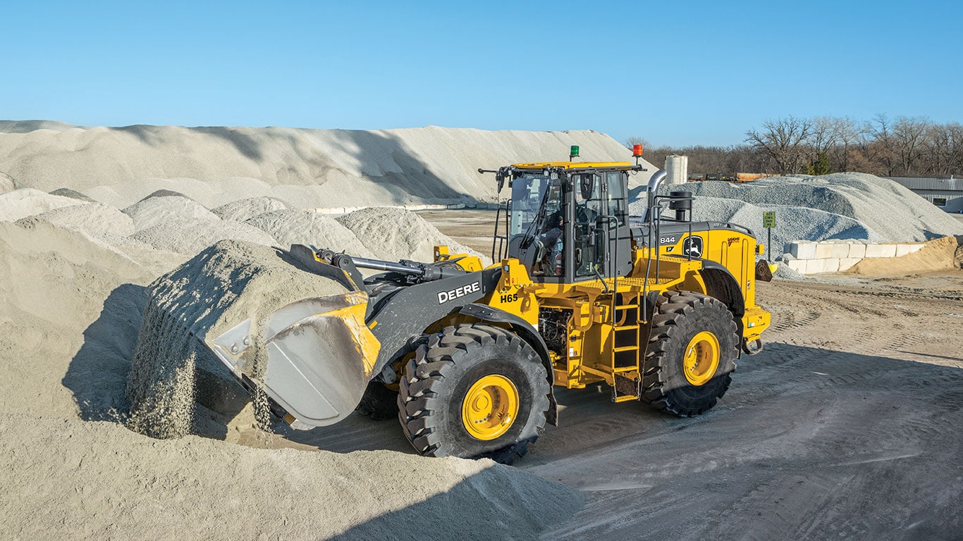 A John Deere 844 P-Tier Loader effortlessly scoops up gravel with its bucket.