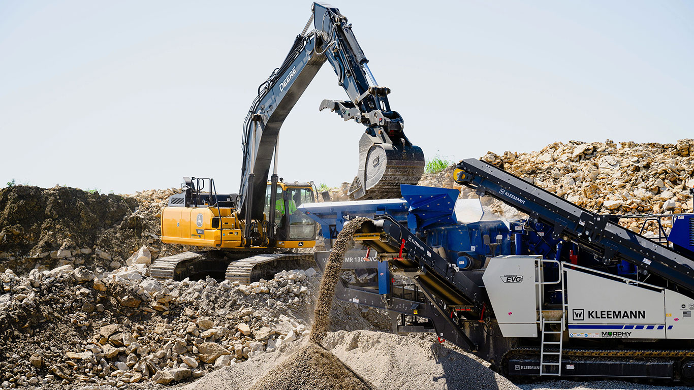 The John Deere 350 P-Tier Excavator easily delivers a load of rock to the Kleemann Mobile Mobirex MR 130i EVO2