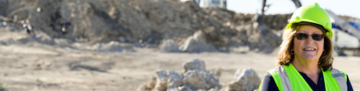 Sandy smiles and looks forward while wearing a hard hat and glasses