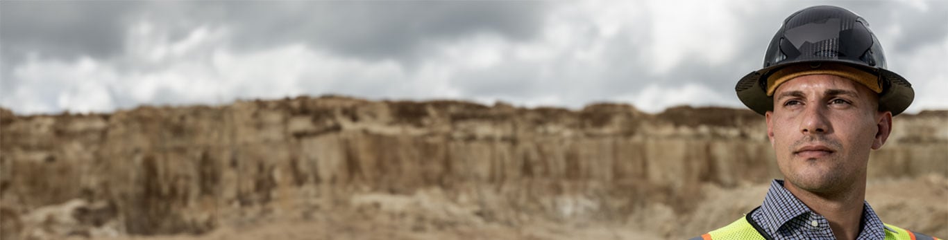 Joey wearing a black hard hat in front of a quarry