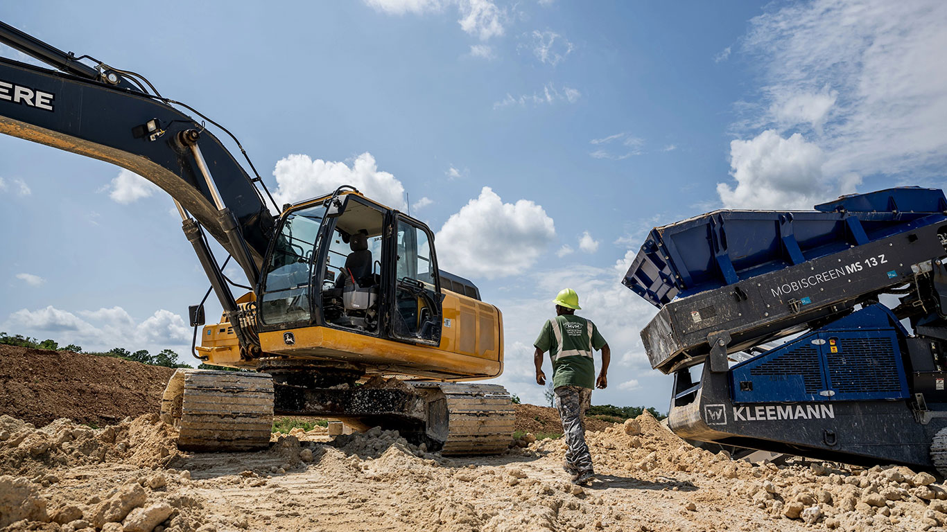 A man wearing a hard hat walking up to an empty excavator