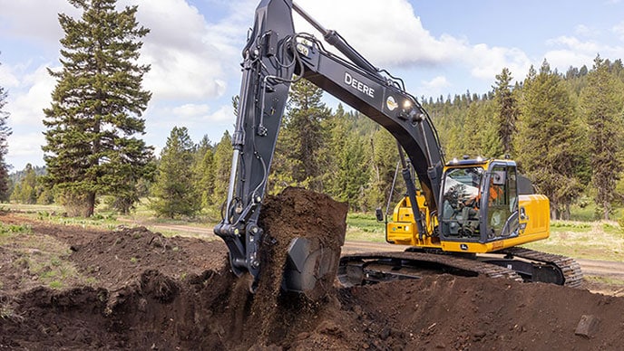 Witness the power of the John Deere 210 P-Tier excavator as it efficiently digs and loads dirt into the 310E.