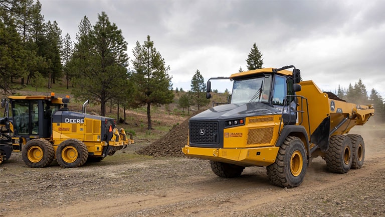 A John Deere 772GP-Tier Motor Grader and Dump Truck on the job site