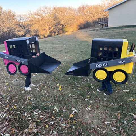 Two children in costumes designed after two John Deere 320E Skid Steer Loaders.