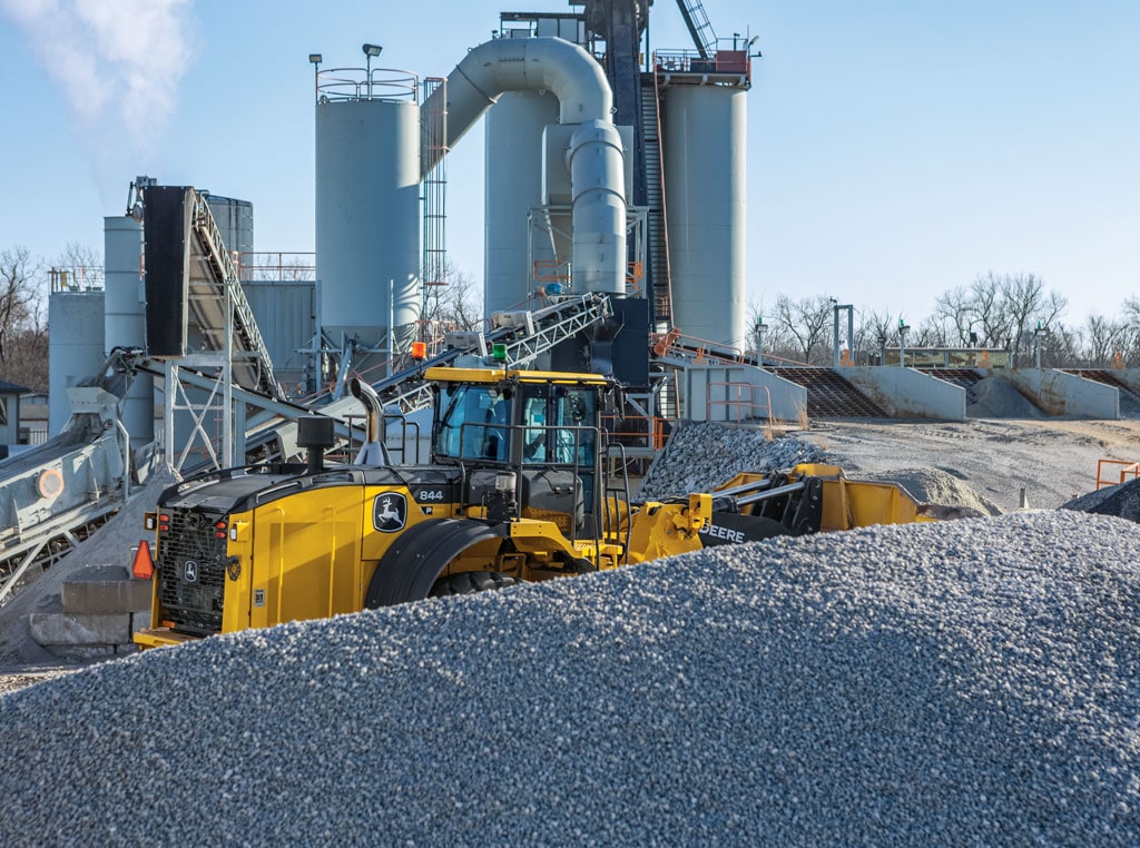A wheel loader moving gravel in front of a large factory