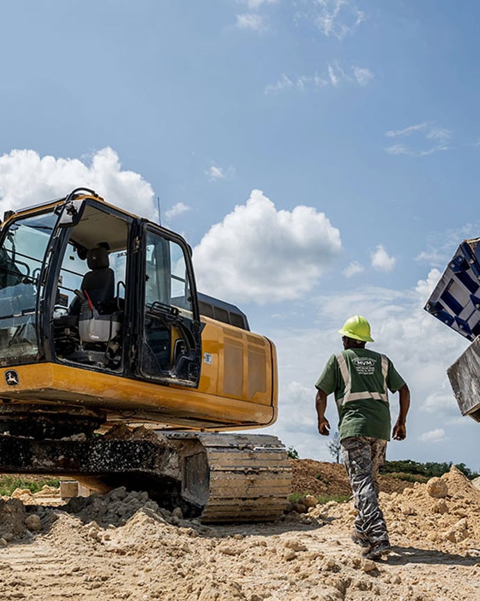 A man wearing a hard hat walking up to an empty excavator