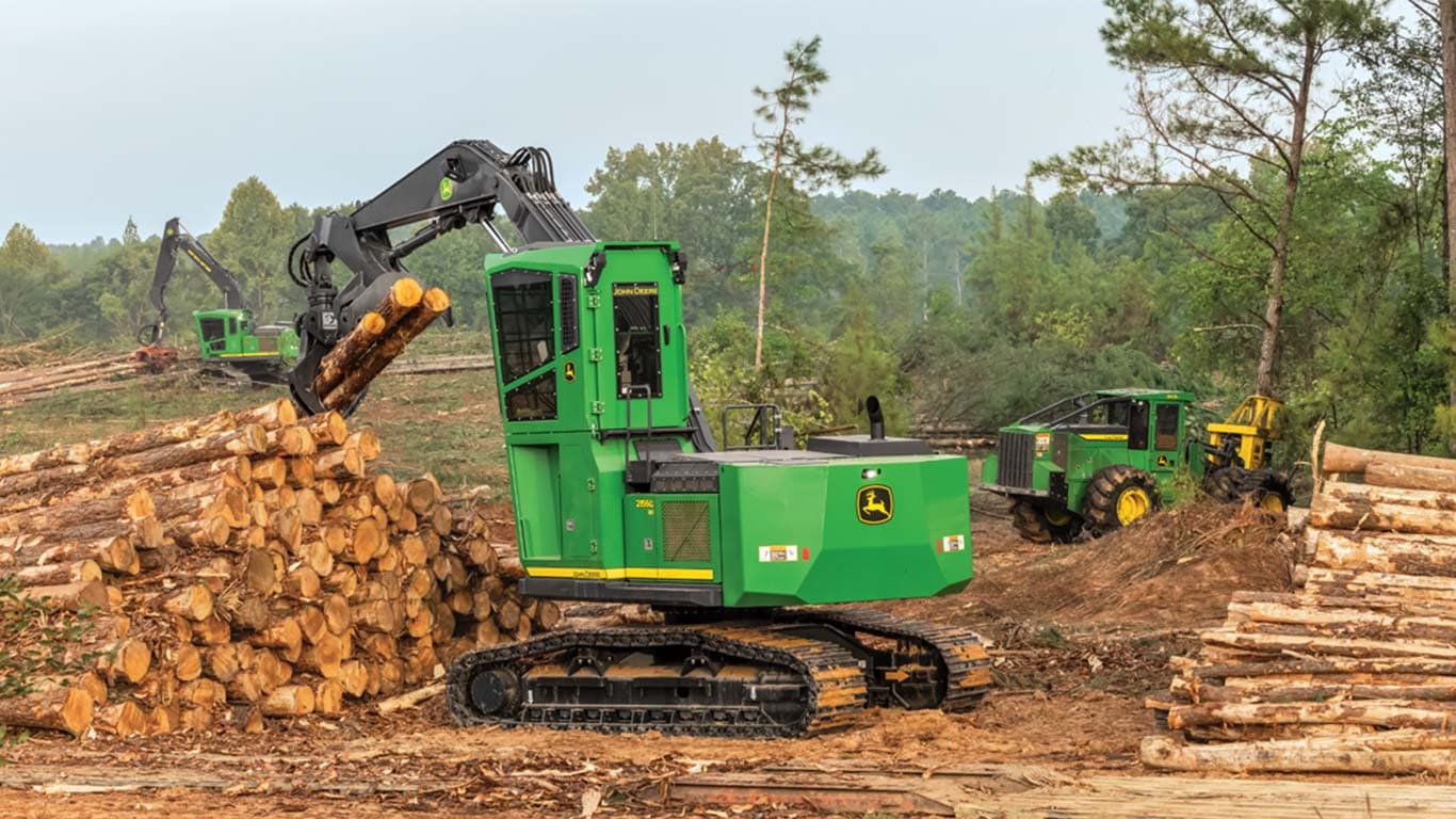 The John Deere 2156G XD grabs logs while the 843L Feller Buncher cuts a tree with its Felling Head.