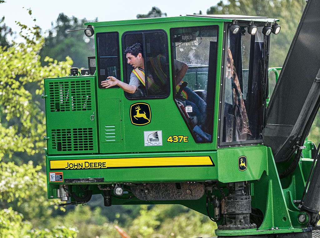 A John Deere 437E Knuckleboom Loader with window open, operator speaking to co-worker