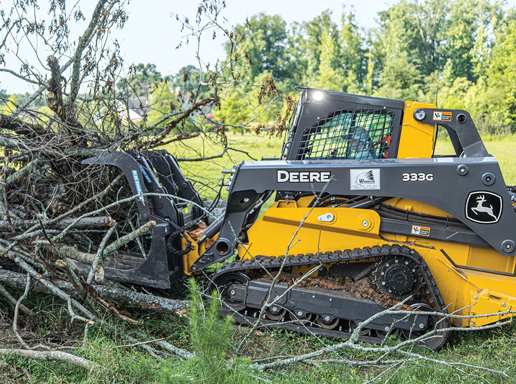 A John Deere 333 G-Tier Compact Track Loader moves a pile of limbs, with a scrap grapple attached.