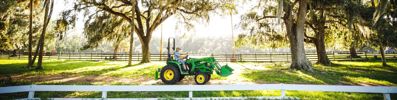 woman on tractor driving along white fencing