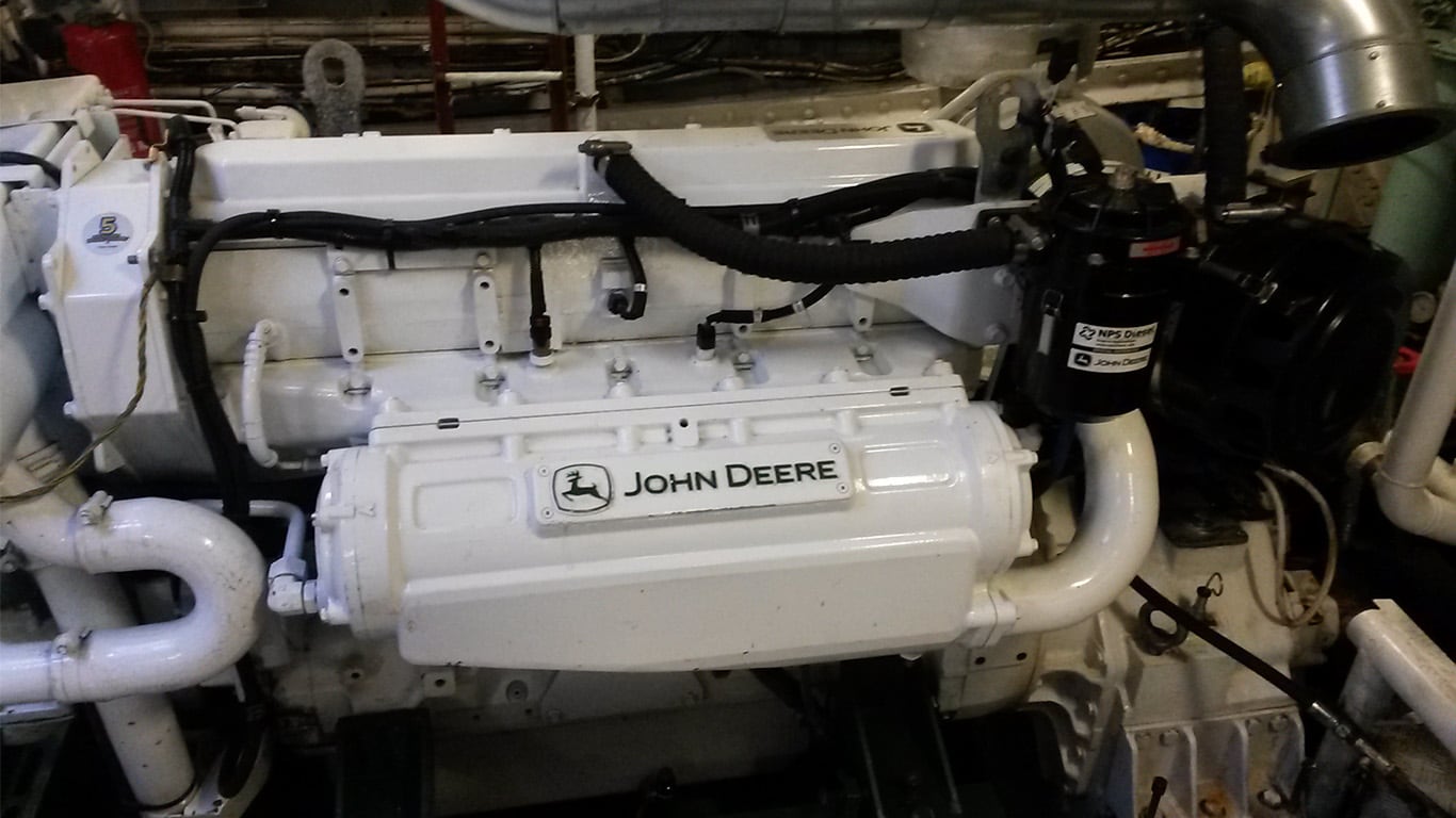 A white John Deere marine engine connected to a ship in an engine room.