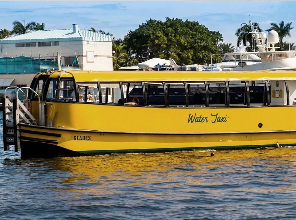 A gold water taxi named ‘Glades’ floating in a harbor on a sunny day.