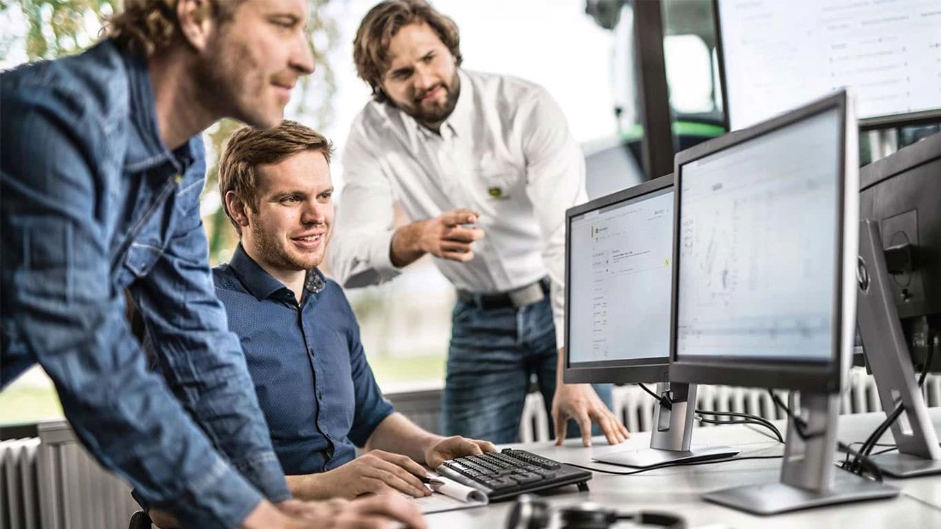 Three service technicians gathered around a computer utilizing John Deere Connected Support