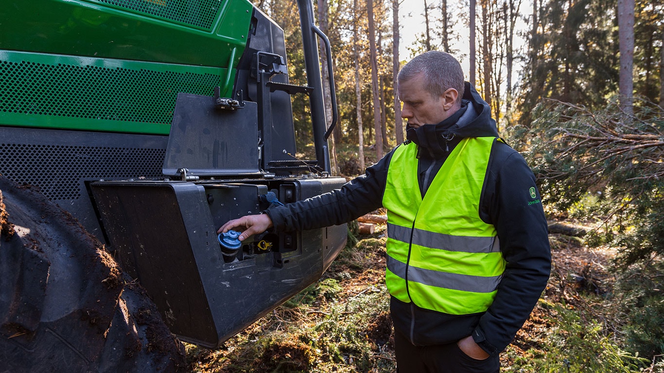 Technician servicing H-Series forestry machine with open engine compartment.