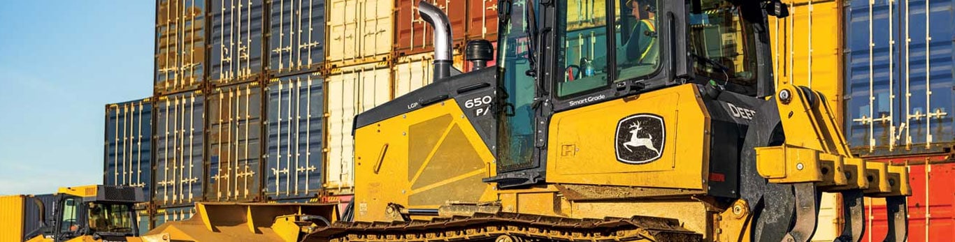 650 P-Tier dozer moves around a jobsite with high stacks of shipping crates in the background