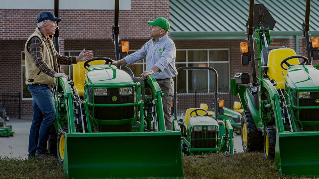 two people standing on either side of a compact utility tractor