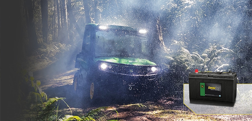 Utility vehicle driving through a wet forest trail with a John Deere StrongBox battery shown in the lower right.