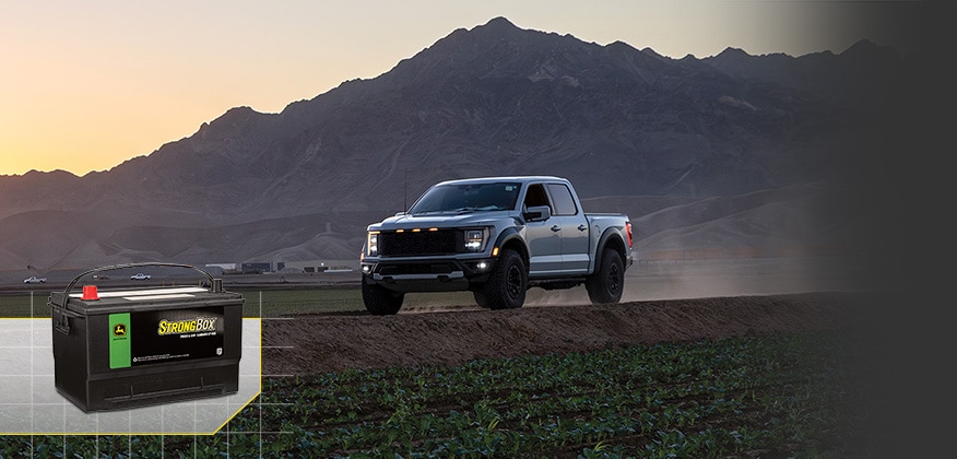 Pickup truck driving along a dirt road with a John Deere StrongBox battery shown in the lower left.