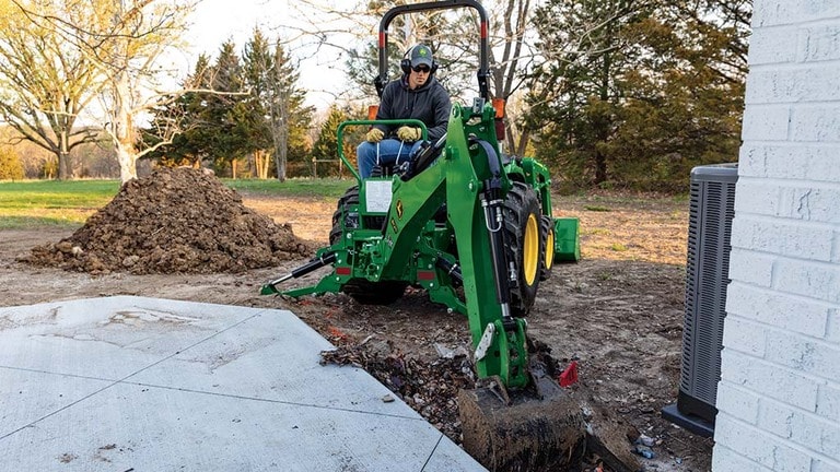 A green backhoe being used to dig a hole near a patio. (11th thumbnail)