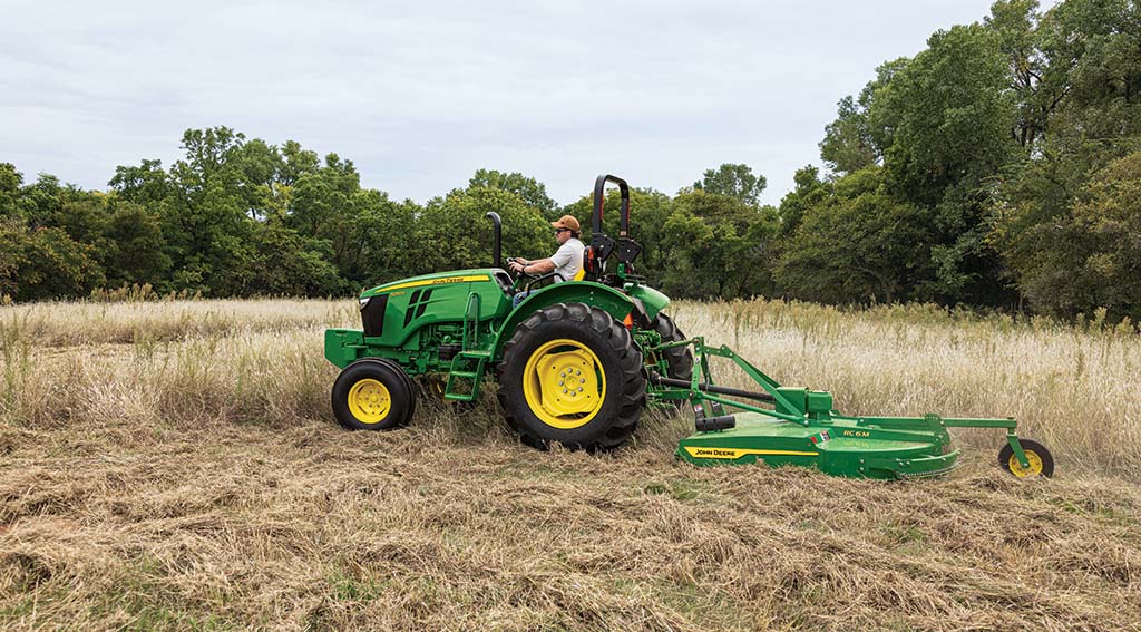 medium-duty series A person driving a compact tractor with a rotary cutter, mowing tall grass in a field