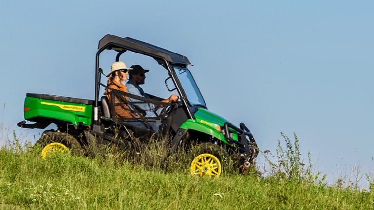 Two people drive a green Gator down a grassy slope under an open sky. (2nd thumbnail)