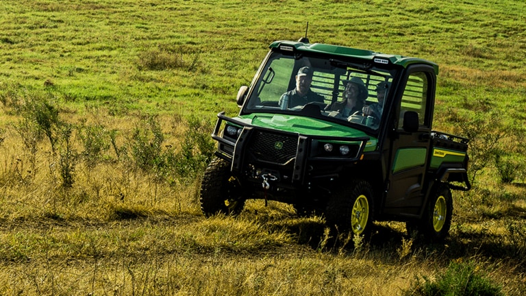 A green cabbed Gator carries three passengers through an open grassy field. (6th thumbnail)