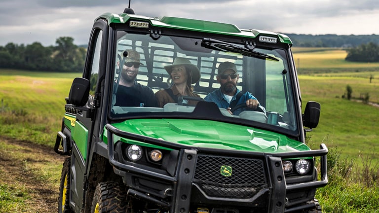 A close-up of a green cabbed Gator carrying three passengers through an open grassy field. (7th thumbnail)