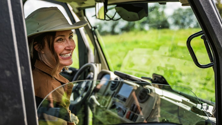 A person in a wide-brimmed hat smiles over the rolled-down window of a cabbed Gator. (8th thumbnail)