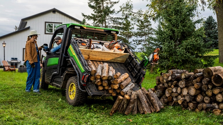 An individual talks to the driver of a Gator through the driver side window while the cargo box tilts up to dump logs. (9th thumbnail)