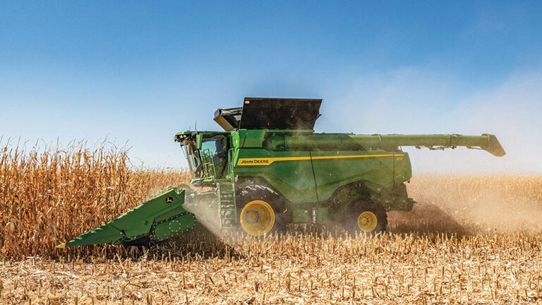 Combine harvester working in a cornfield, with dust rising against a clear blue sky. Harvest in progress. (3rd thumbnail)