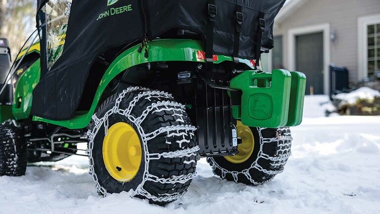 Close-up of snow chains around the back tires of a green riding mower. (5th thumbnail)