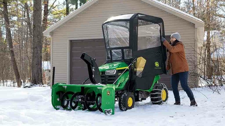 A green riding mower in snow with a snow blower and weather encloser attached to it. (8th thumbnail)