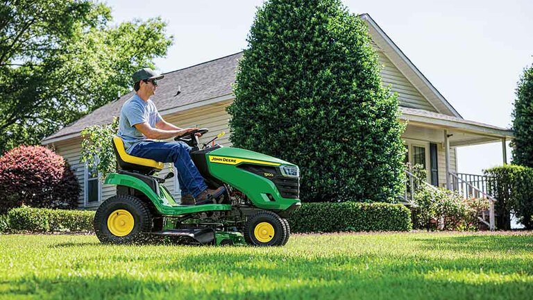 Right-side view of a person driving a green riding mower with grass clippings coming out the side. (7th thumbnail)