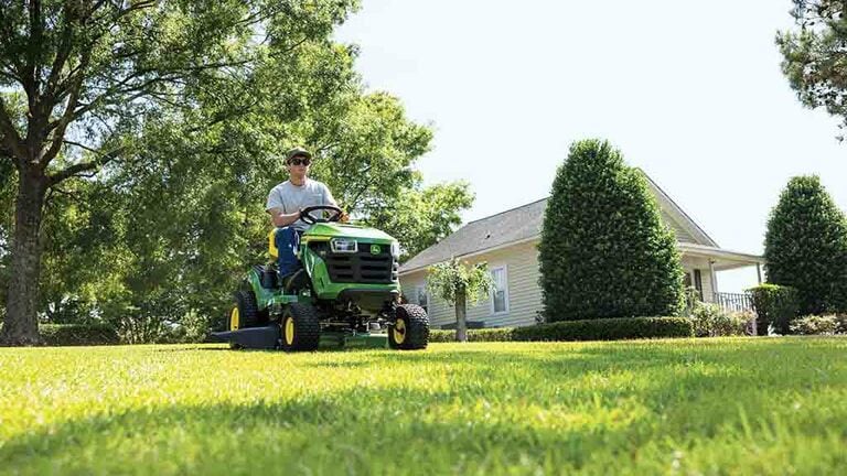 A person driving a green riding mower over a flat open lawn. (5th thumbnail)